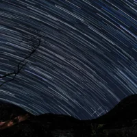 Vitor Cerqueira - Star Trail realizado na Lapinha da Serra (MG), com o Pico da Lapinha (esquerda) e Pico do Breu (direita) ao fundo, bem como três meteoros com trajetórias coincidentes no canto inferior direito.
